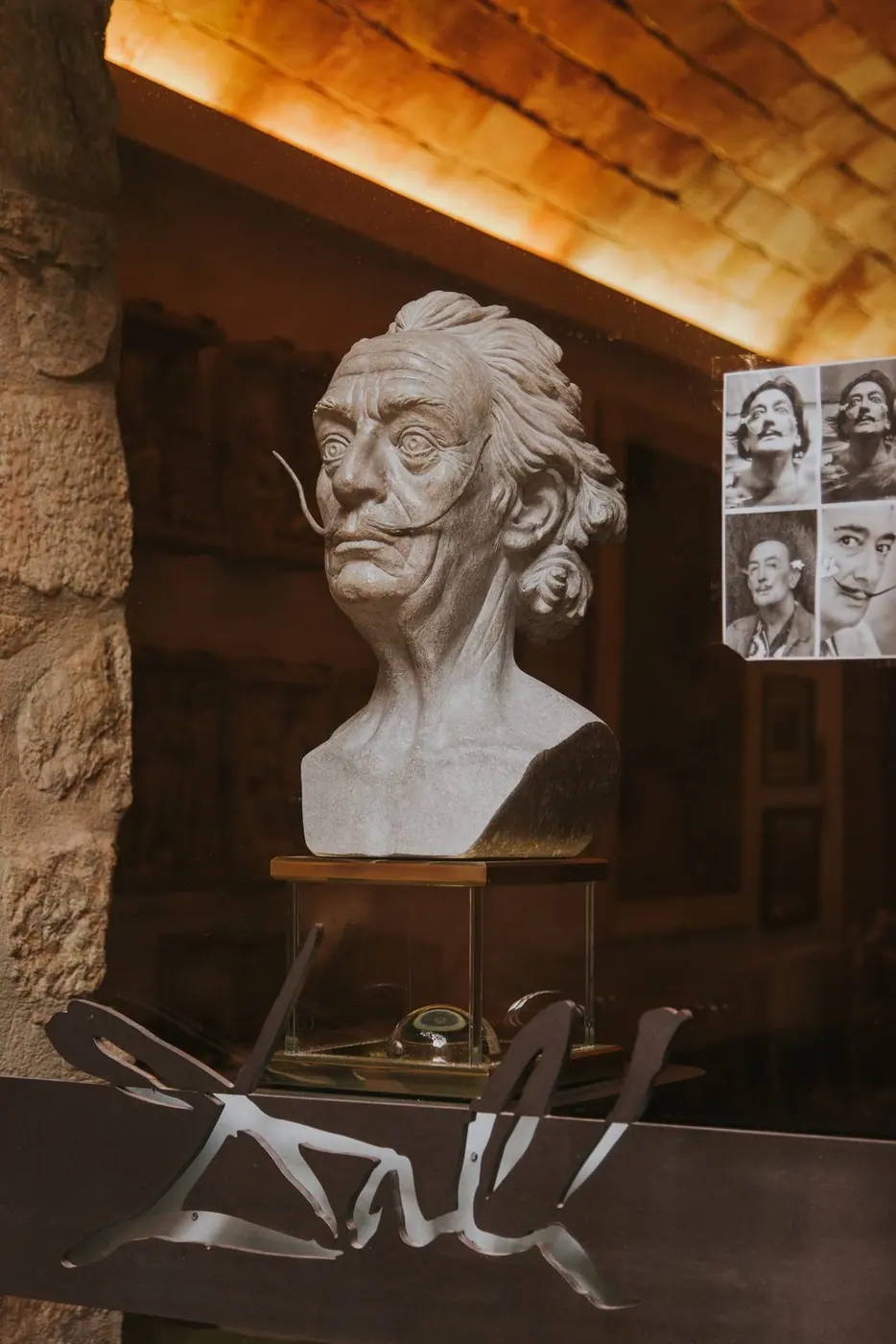 Busto de Salvador Dalí tras un ventanal del Hotel-Museu Llegendes, con su firma en metal